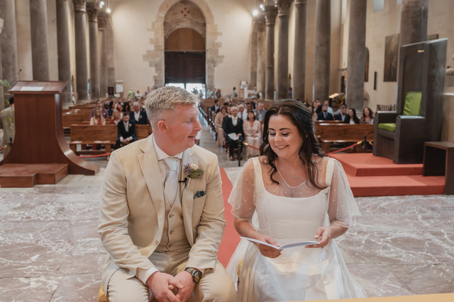 Gráinne and Phil seated, reading their vows in the cathedral