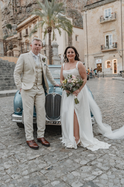 Gráinne and Phil posing with a vintage powder-blue car in Cefalù, Sicily