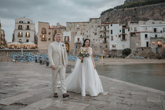 Gráinne and Phil on the Cefalù waterfront promenade with the beach and La Rocca behind