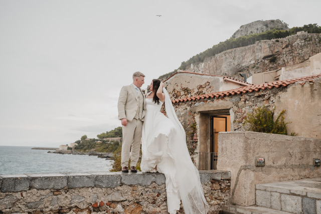 Gráinne and Phil kissing on a stone wall above the sea in Cefalù, Sicily