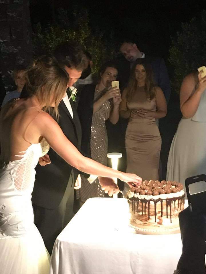 Bride and groom cutting their wedding cake together at an elegant evening Sicilian reception surrounded by guests