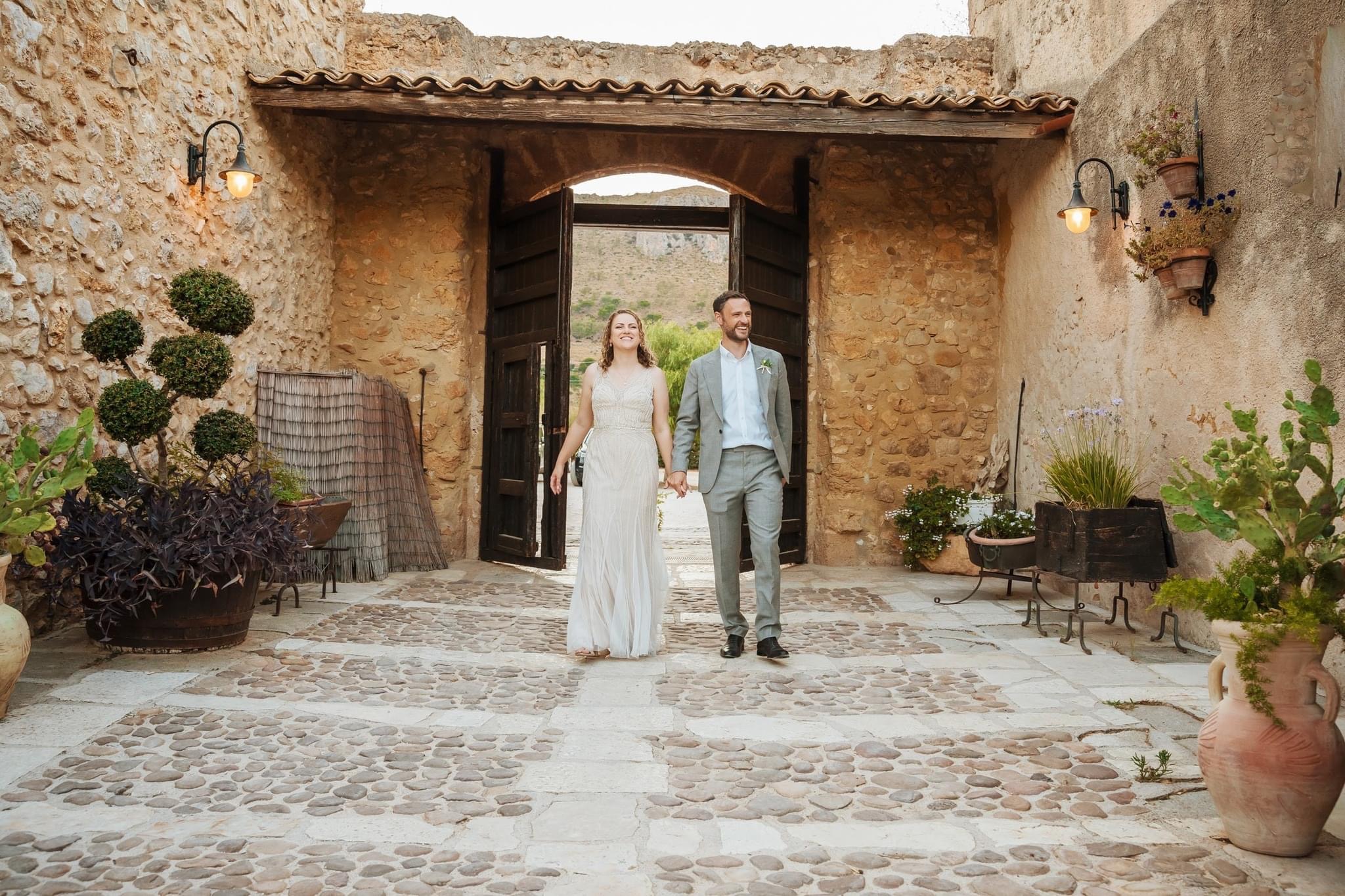 Bride and groom walking hand in hand along a stone garden pathway, the bride trailing a long flowing gown train