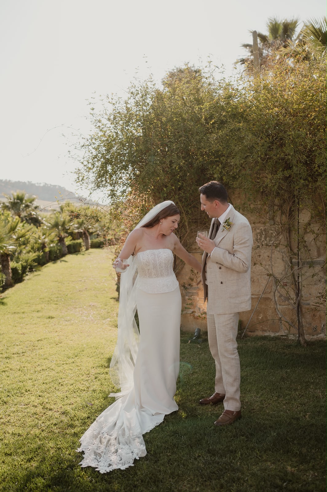 Bride and groom sharing a tender moment in a sunlit Sicilian garden during golden hour, the groom in a cream linen suit