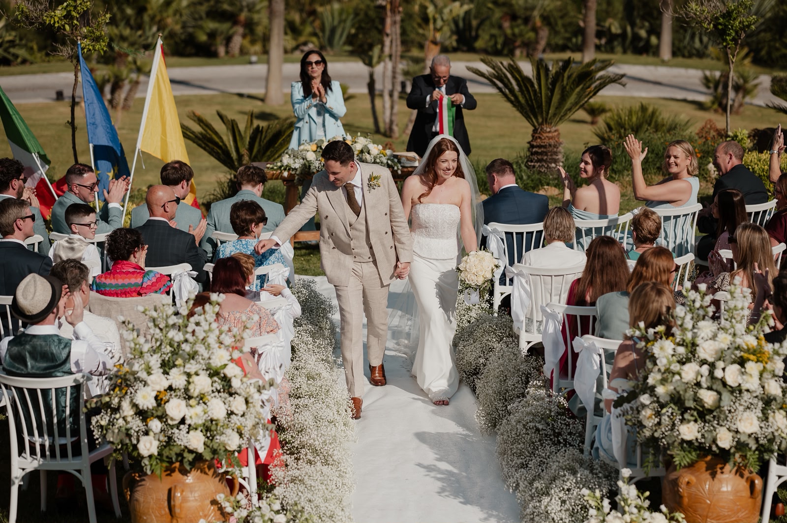 Joyful recessional with guests waving flags after a Sicilian ceremony