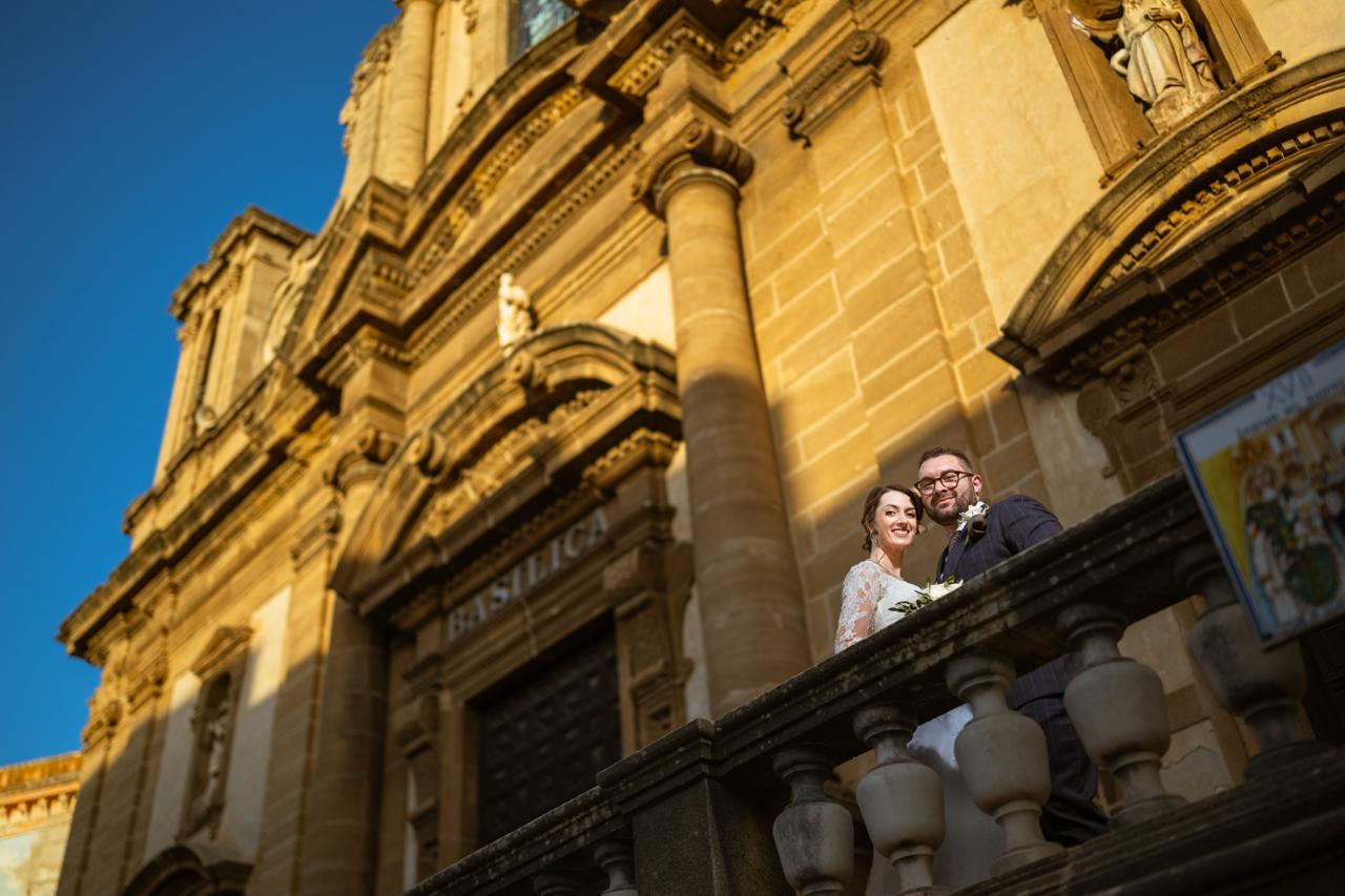 Bride and groom on the stone balcony of the Basilica in Sciacca against a blue sky