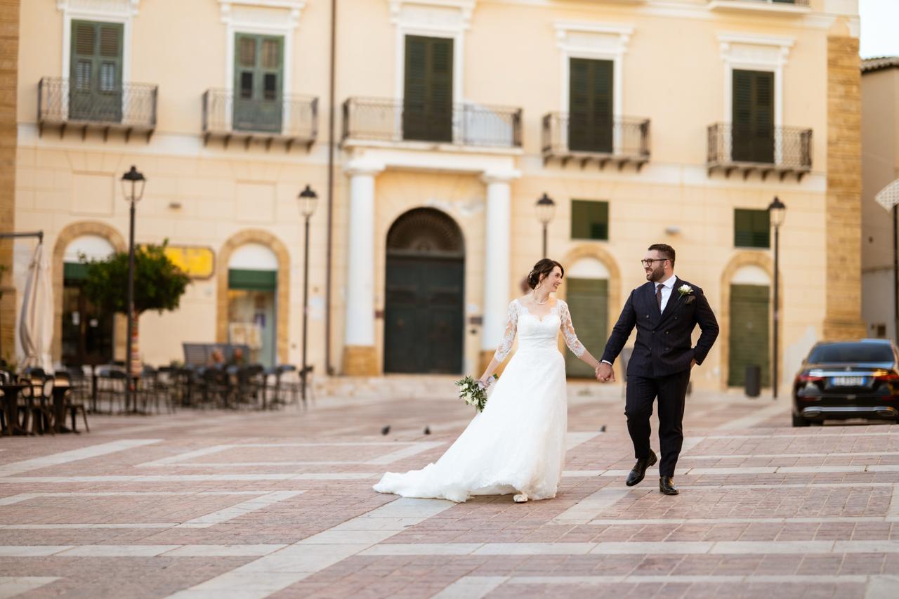 Isabella and Billy walking hand in hand across a sunlit piazza in Sciacca