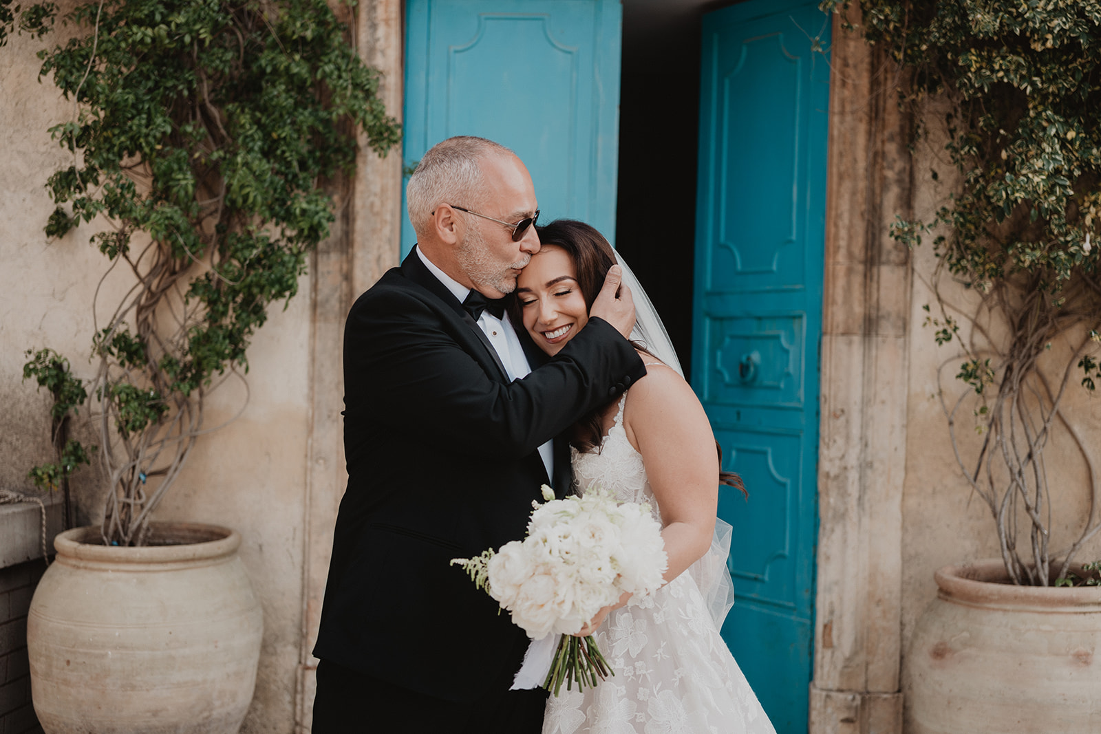 Lidia sharing a tender embrace with her father beside a turquoise door