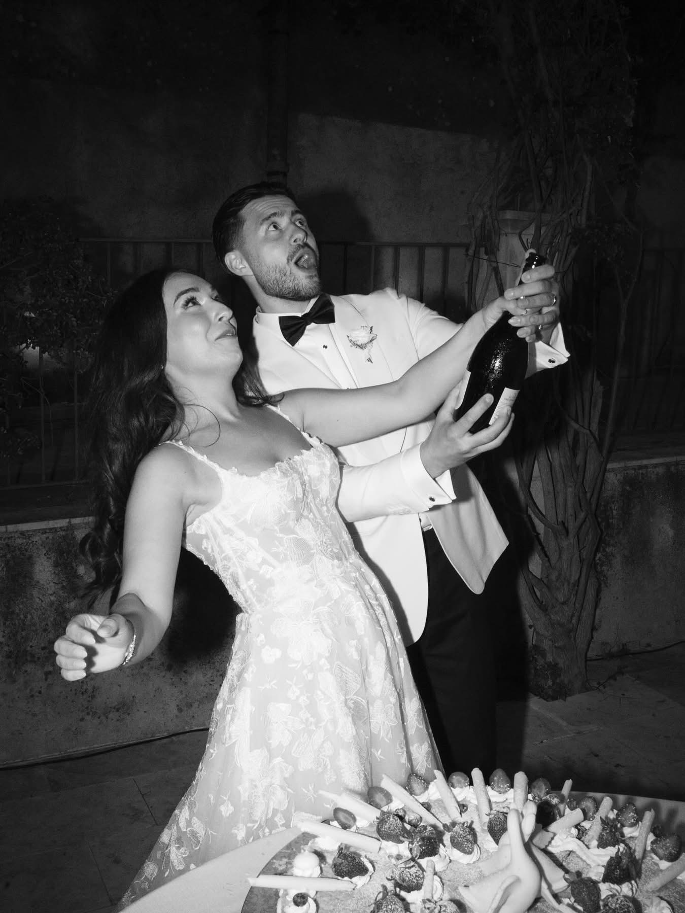 A black-and-white photo of champagne popping over the millefoglie-style wedding cake