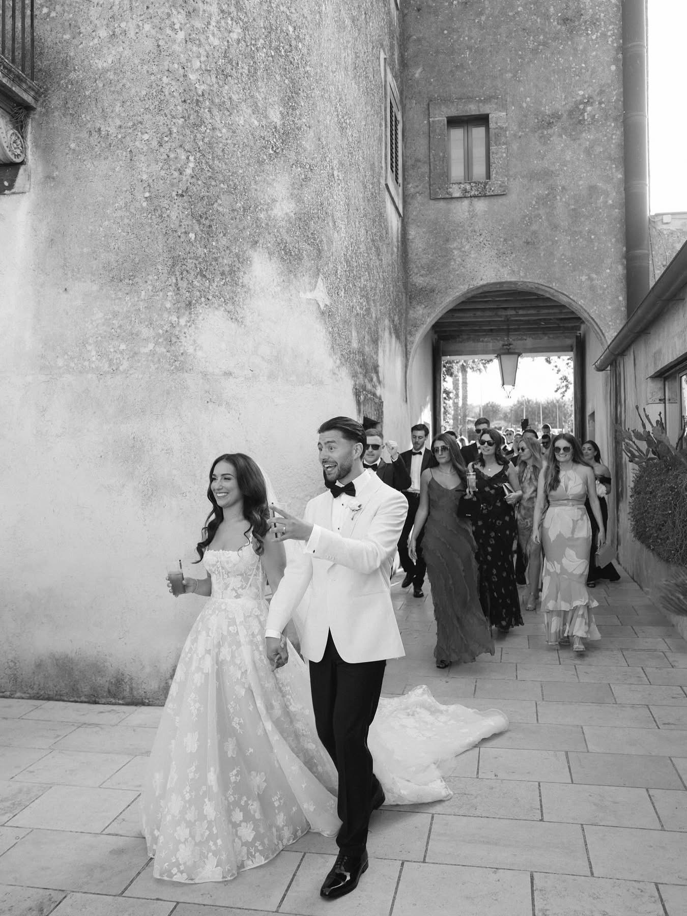 A black-and-white photo of Lidia and Rian walking through the courtyard with their guests