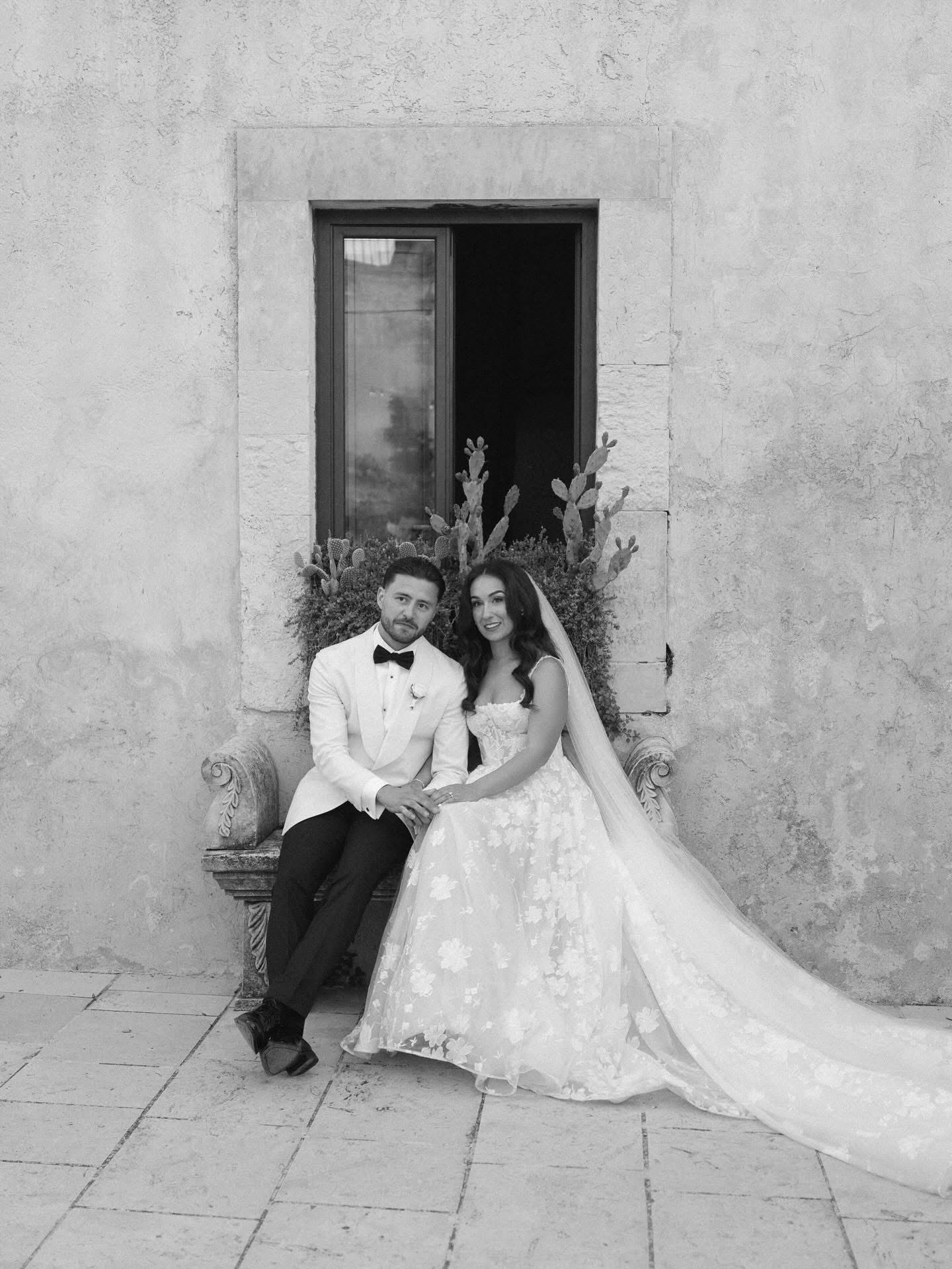 A black-and-white photo of Lidia and Rian on a stone bench among cacti