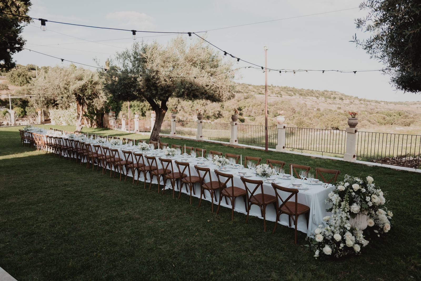 An alfresco imperial wedding table with white flowers and festoon lights on the lawn at Borgo del Carato