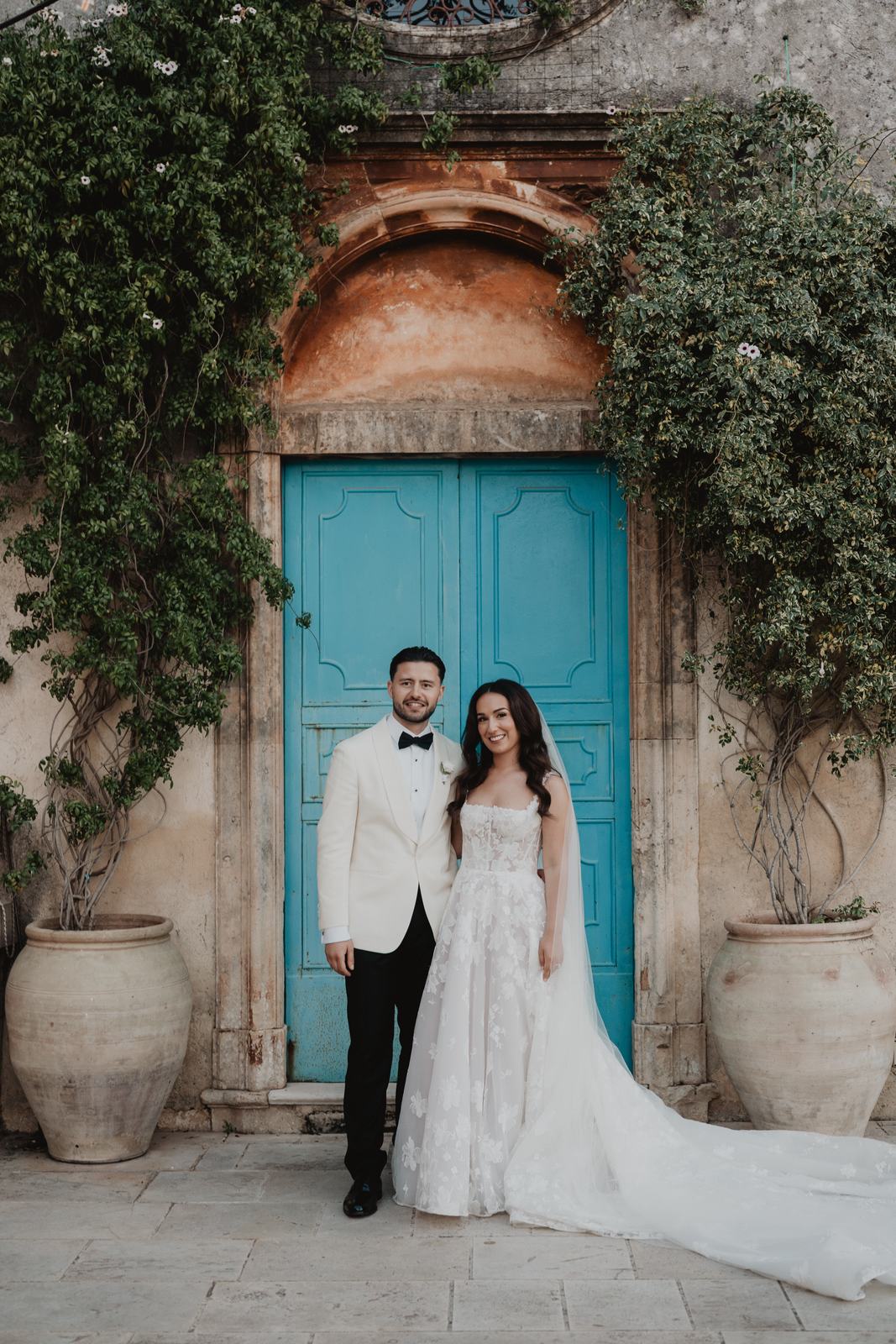 A bride and groom beside an ivy-framed blue door at Borgo del Carato, a farmhouse wedding venue in Sicily