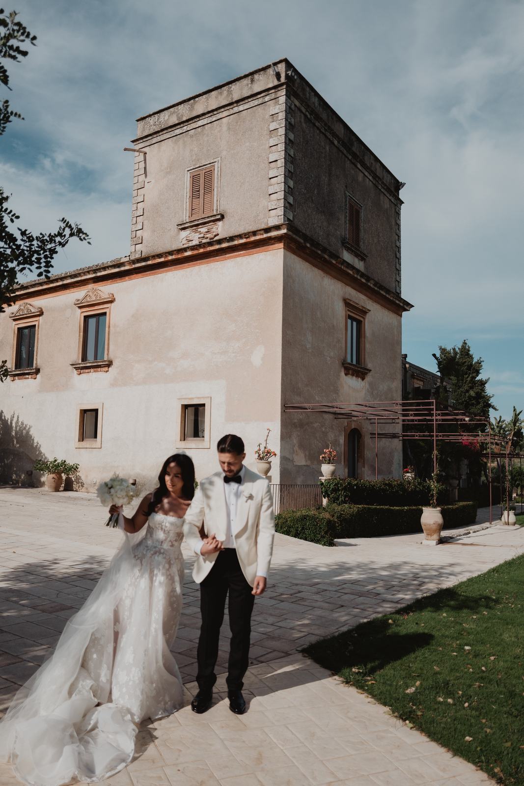 A bride and groom in front of the stone villa and tower at Borgo del Carato in south-east Sicily