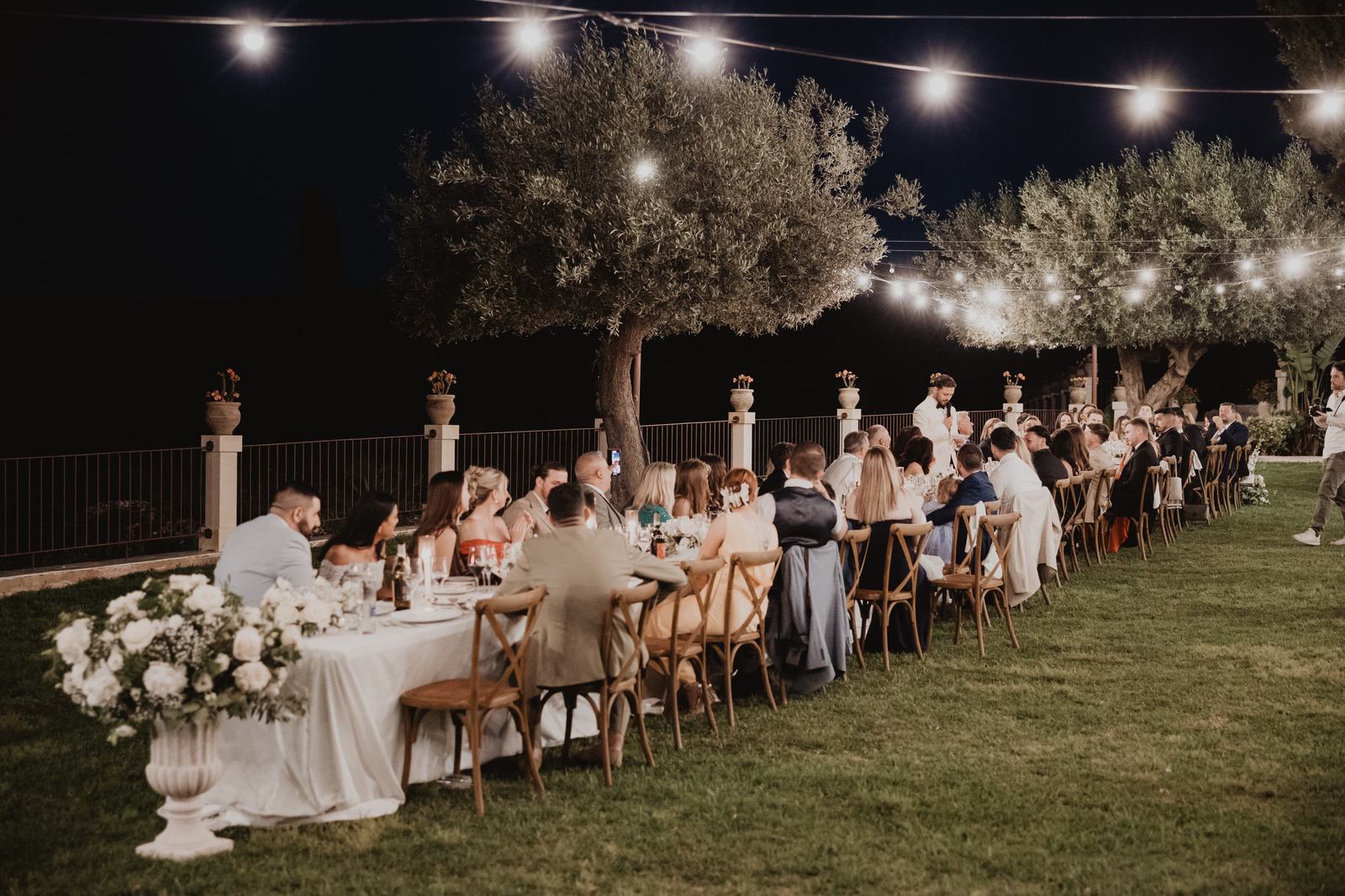 Wedding guests dining under festoon lights at a long table at Borgo del Carato after dark