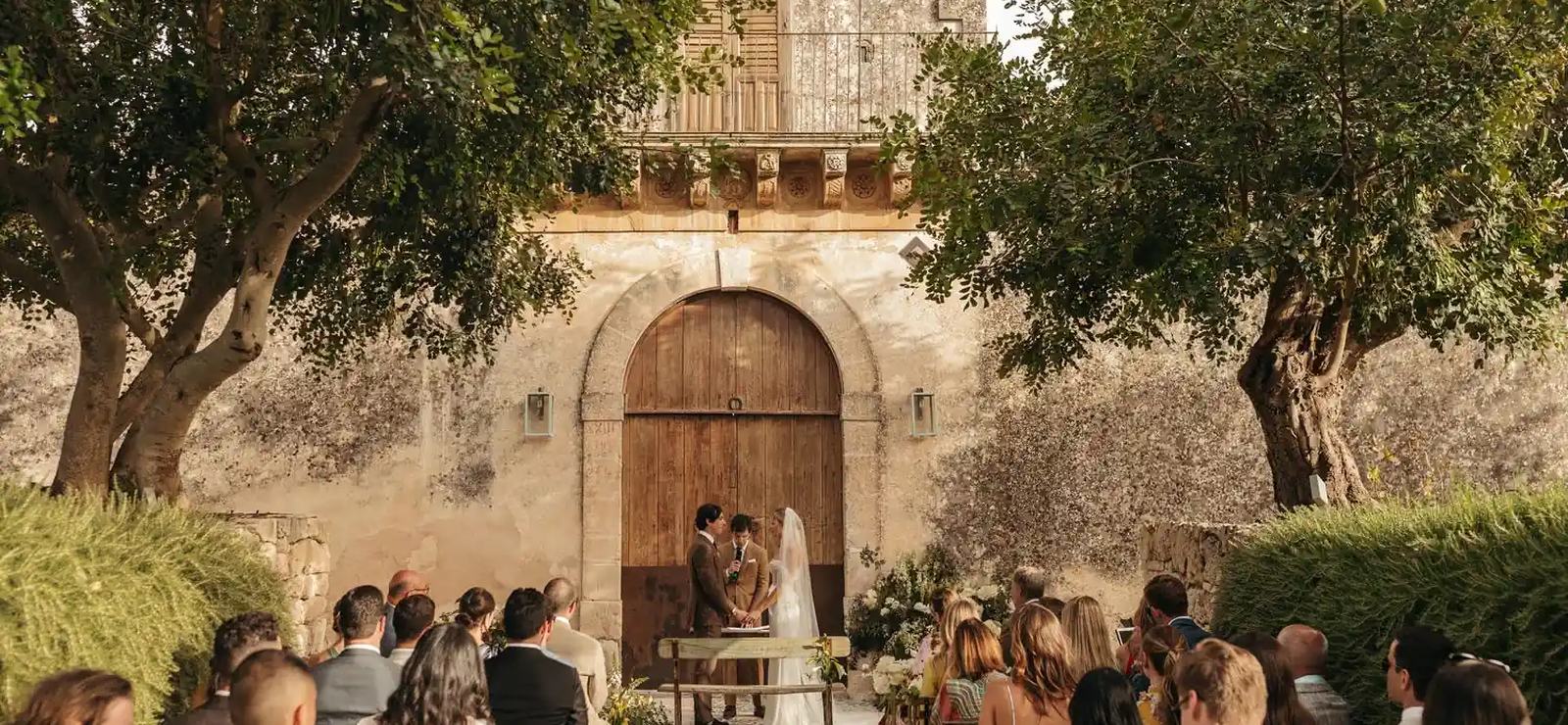 A wedding ceremony in front of the old wooden door of the manor house at Dimora delle Balze, near Noto