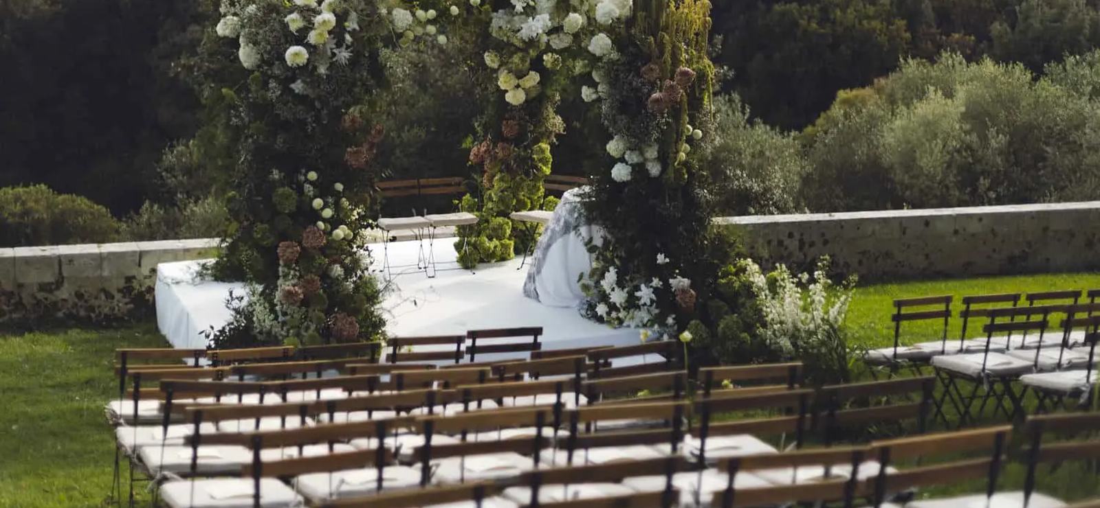 An outdoor wedding ceremony set up with white flowers and chairs in the garden at Dimora delle Balze, with the valley beyond