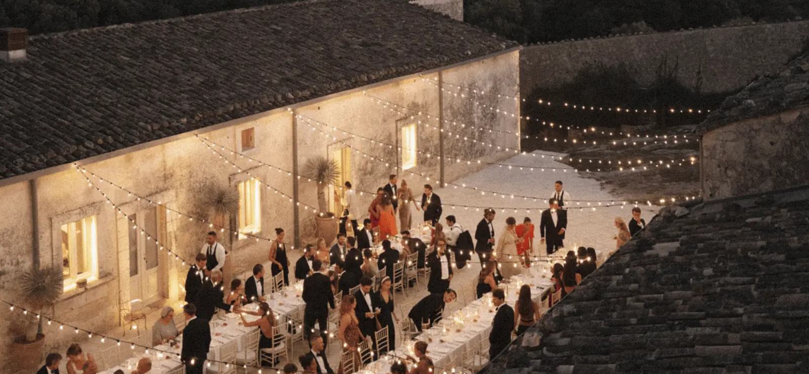 Wedding guests at long tables in the courtyard of Dimora delle Balze at dusk, under string lights