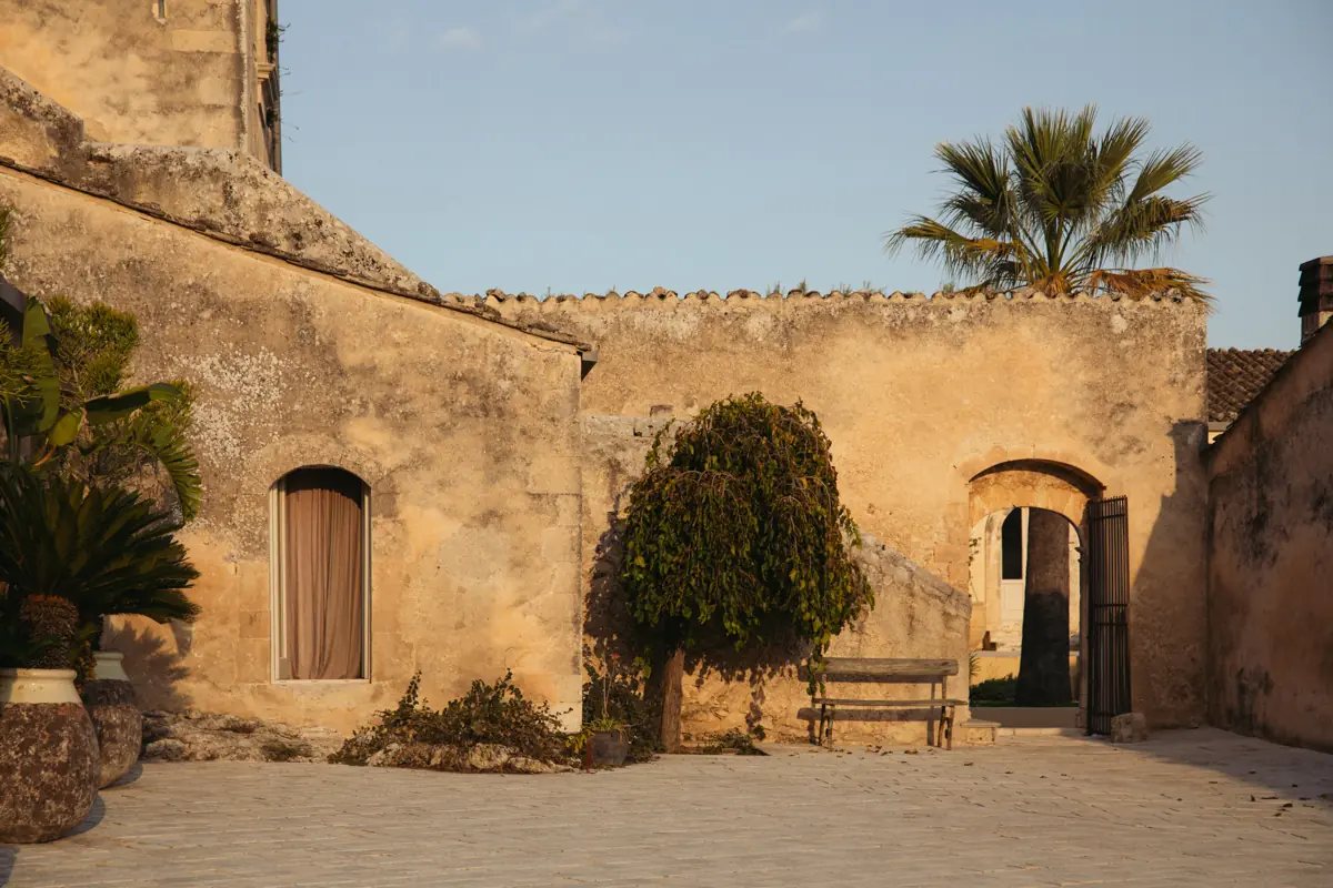 The main courtyard of the restored masseria at Dimora delle Balze, with honey-coloured stone walls and a palm tree