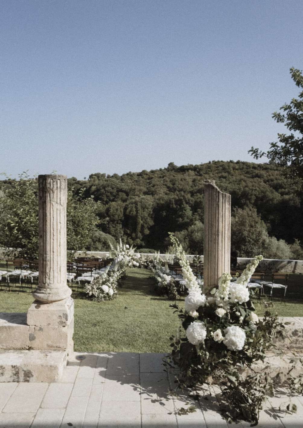 Wedding ceremony set-up among ancient stone columns with white flowers and a view over the valley at Dimora delle Balze