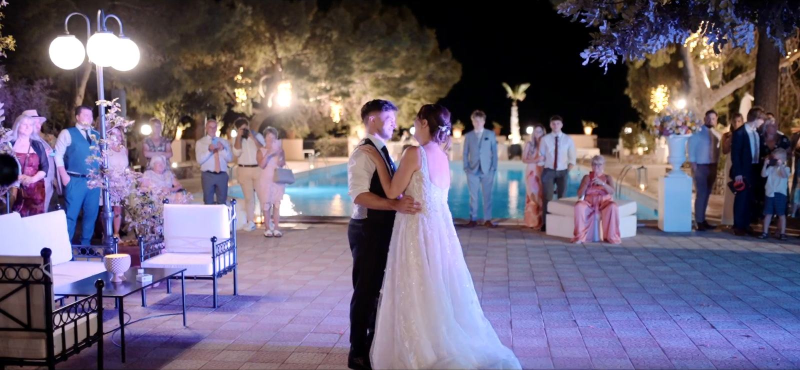 A bride and groom sharing their first dance in the gardens of the Excelsior Palace, with the lit pool behind them