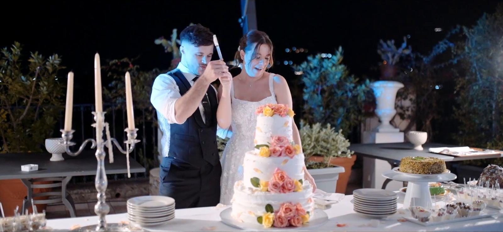 A bride and groom cutting their wedding cake in the gardens of the Excelsior Palace on a September evening